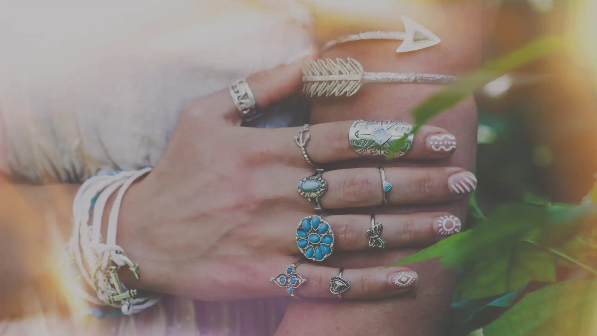 Hand adorned with numerous silver rings, including a prominent turquoise ring and an arrow-shaped bracelet.