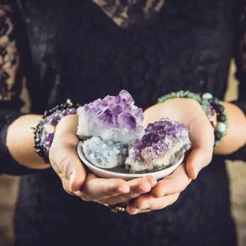 Hands holding a small dish with various amethyst crystals.